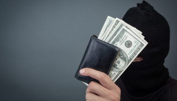 Black criminals wear a head yarn, hold a dollar card on a gray background.